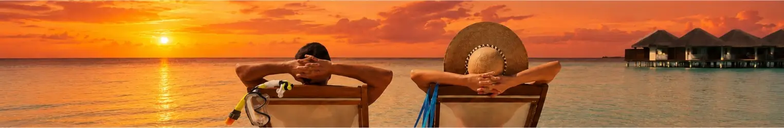 A couple relaxing on the beach enjoying a stunning orange sunset over calm ocean waters at a tropical travel destination.