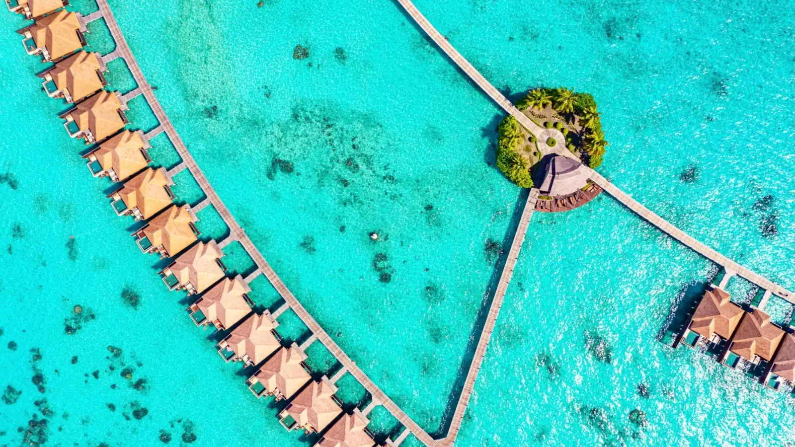 Aerial view of luxury overwater villas and wooden boardwalks over clear blue ocean water at Ayada Maldives resort.