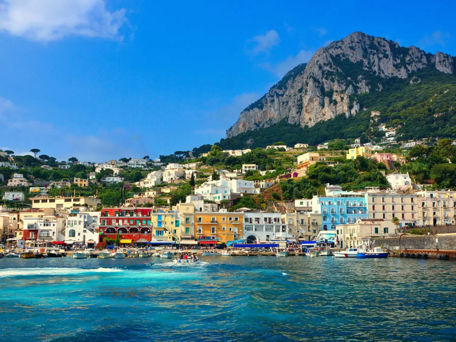 Marina Grande on the island of Capri, with its colorful buildings and the dramatic limestone cliffs of Monte Solaro rising in the background.
