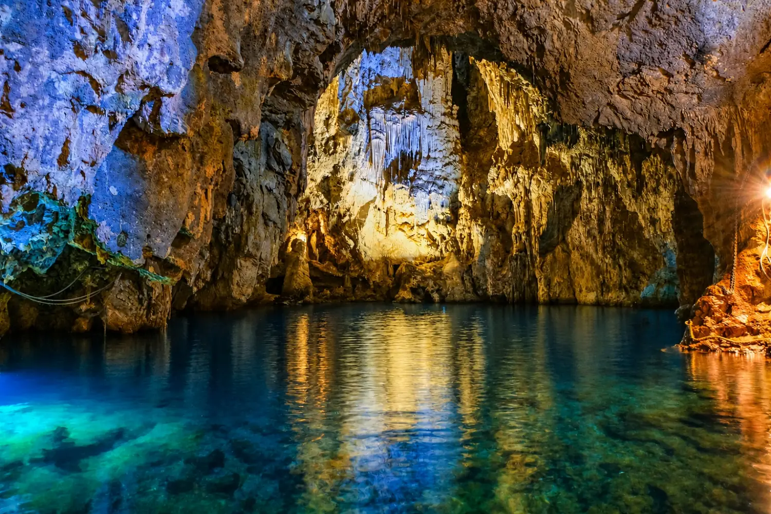 Interior view of the Emerald Grotto sea cave in Conca dei Marini along the Amalfi Coast, Italy, featuring glowing blue water and limestone stalactites.