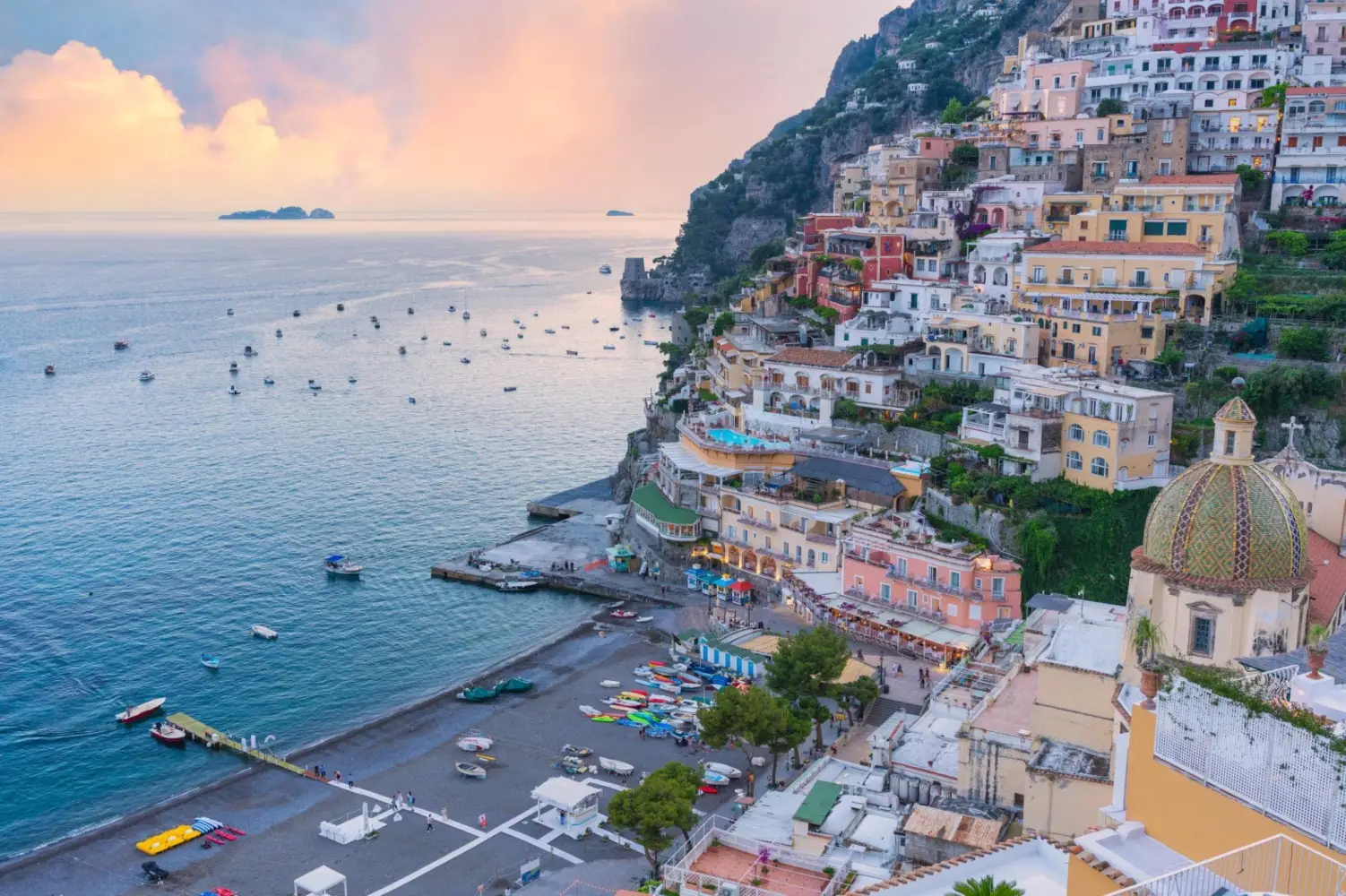 The iconic pastel-colored buildings of Positano, Italy, built into the steep cliffs of the Amalfi Coast at sunset.