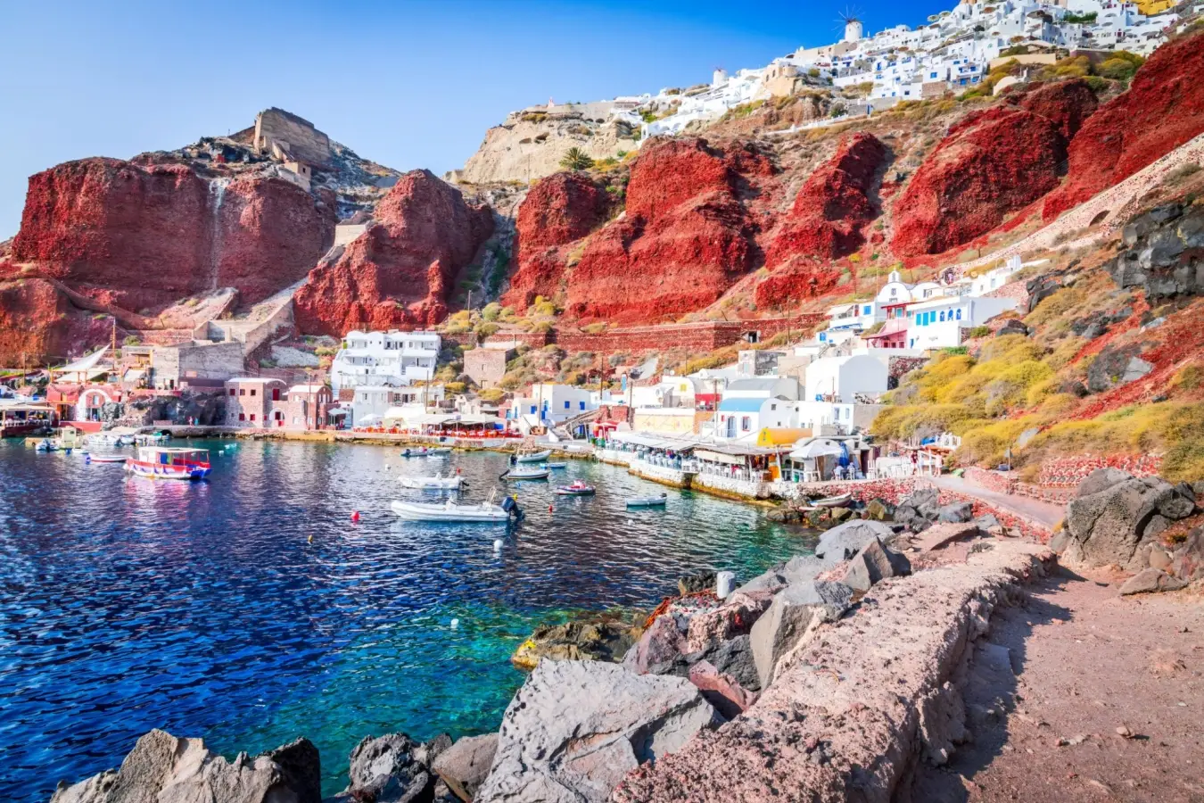 Waterfront seafood restaurants and fishing boats at Ammoudi Bay under the red cliffs of Santorini Greece.