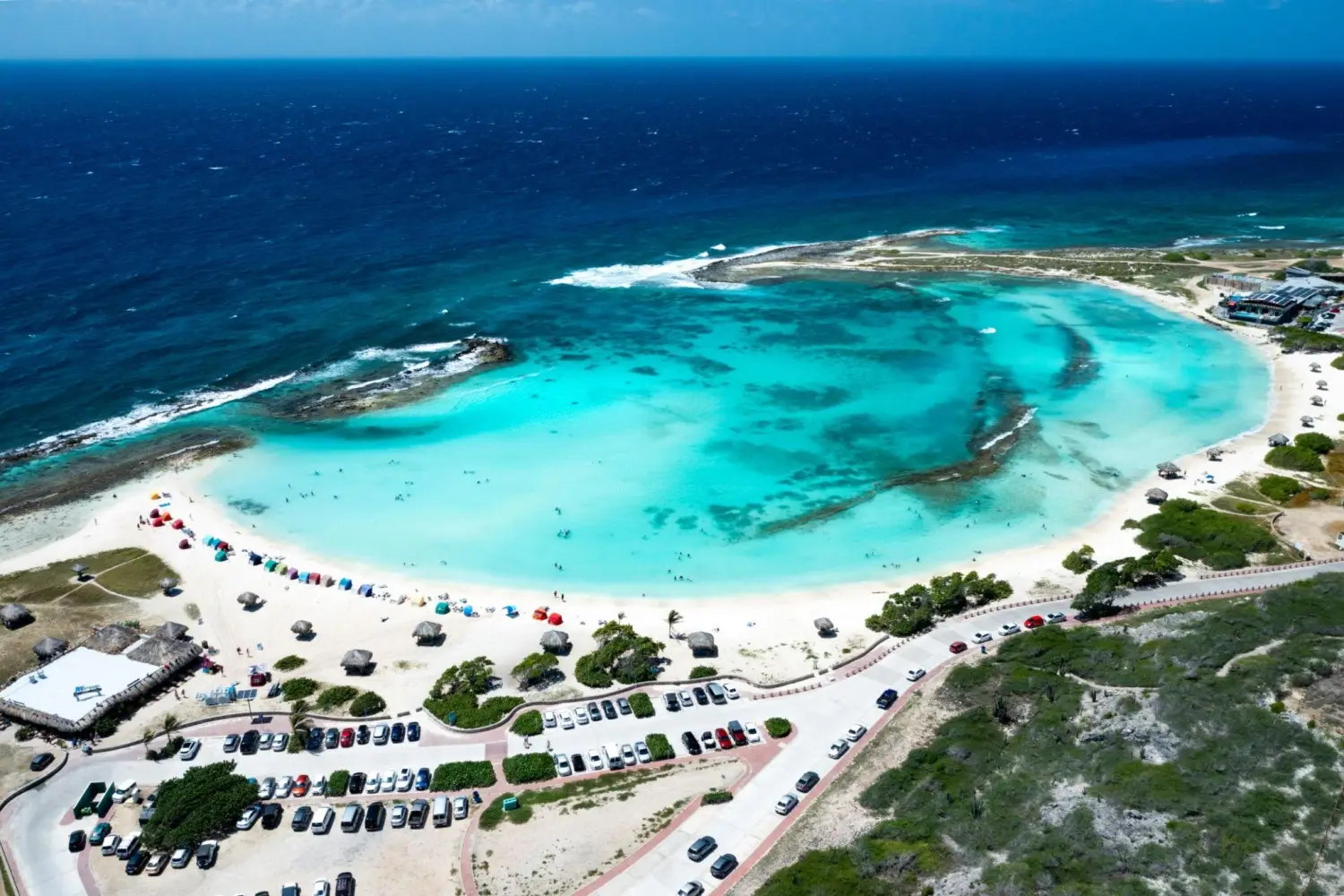 An aerial view of the crescent-shaped lagoon, white sand, and turquoise waters at Baby Beach in Aruba.