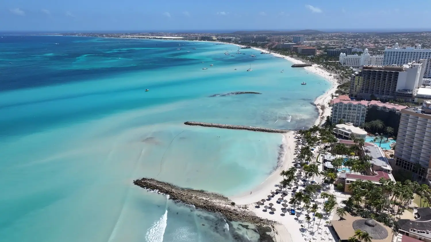 Aerial view of Palm Beach in Aruba featuring turquoise Caribbean water, white sand, and beachfront high-rise resort hotels.