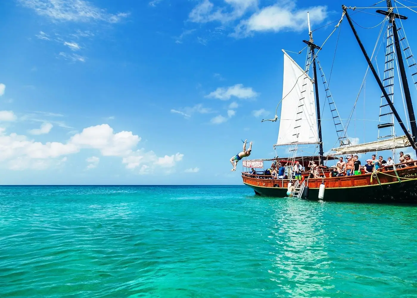 Tourist doing a backflip while rope swinging into the ocean from a Jolly Pirates pirate ship schooner in Aruba.