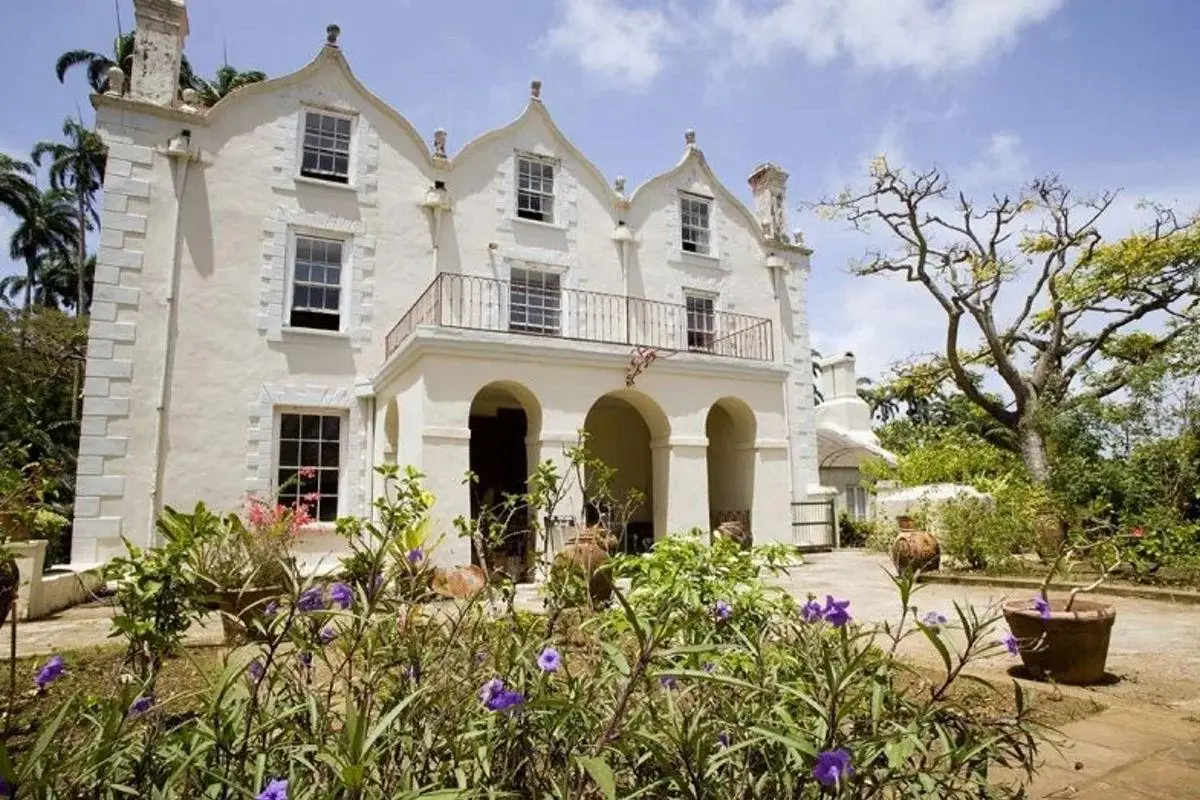 St. Nicholas Abbey historic plantation house in Barbados featuring white Jacobean architecture with curvilinear gables and a blooming flower garden in the foreground.