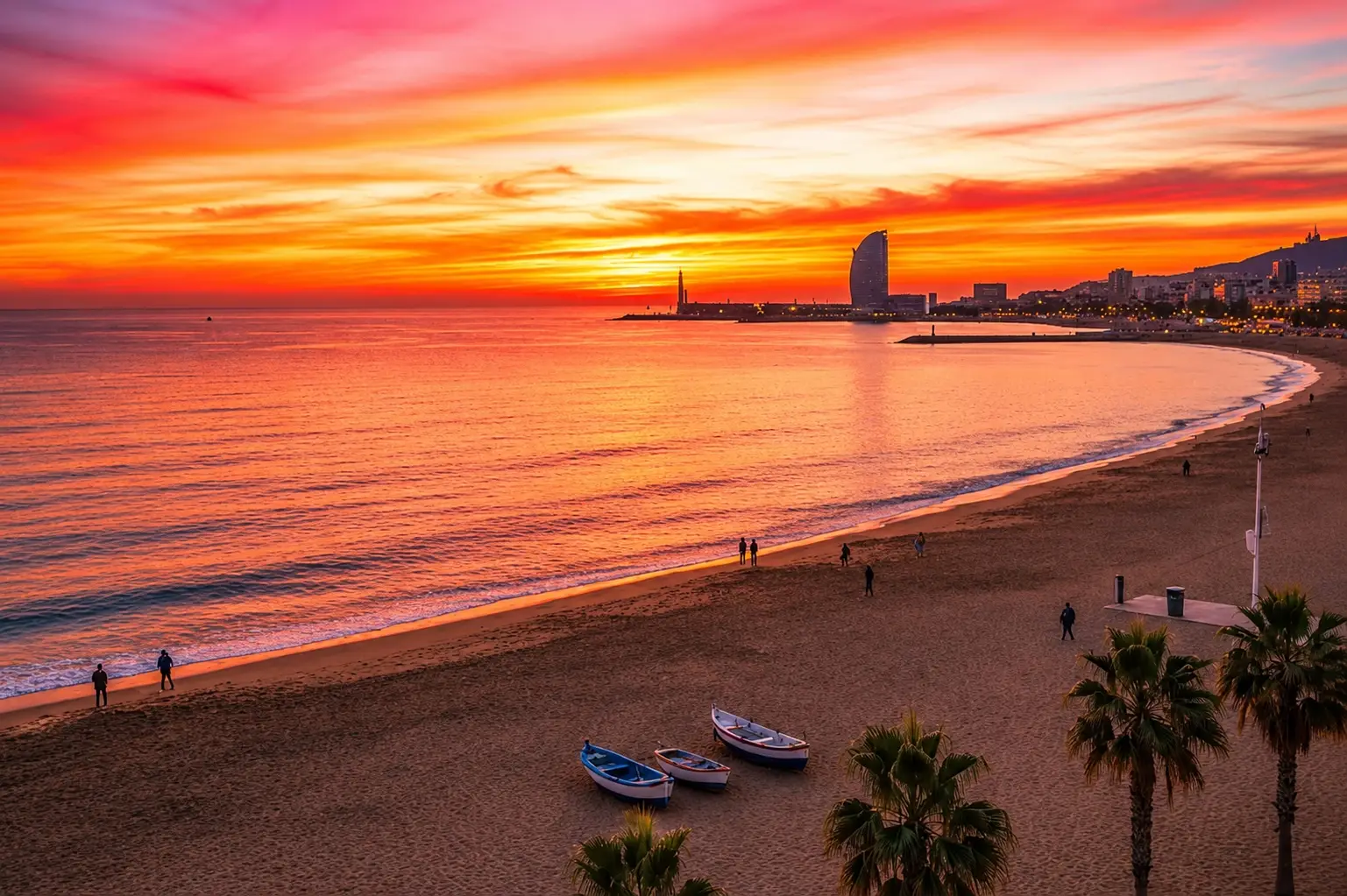 Vibrant orange and pink sunrise over Barceloneta Beach in Barcelona, Spain with small boats on the sand and the sail-shaped W Hotel in the distance.