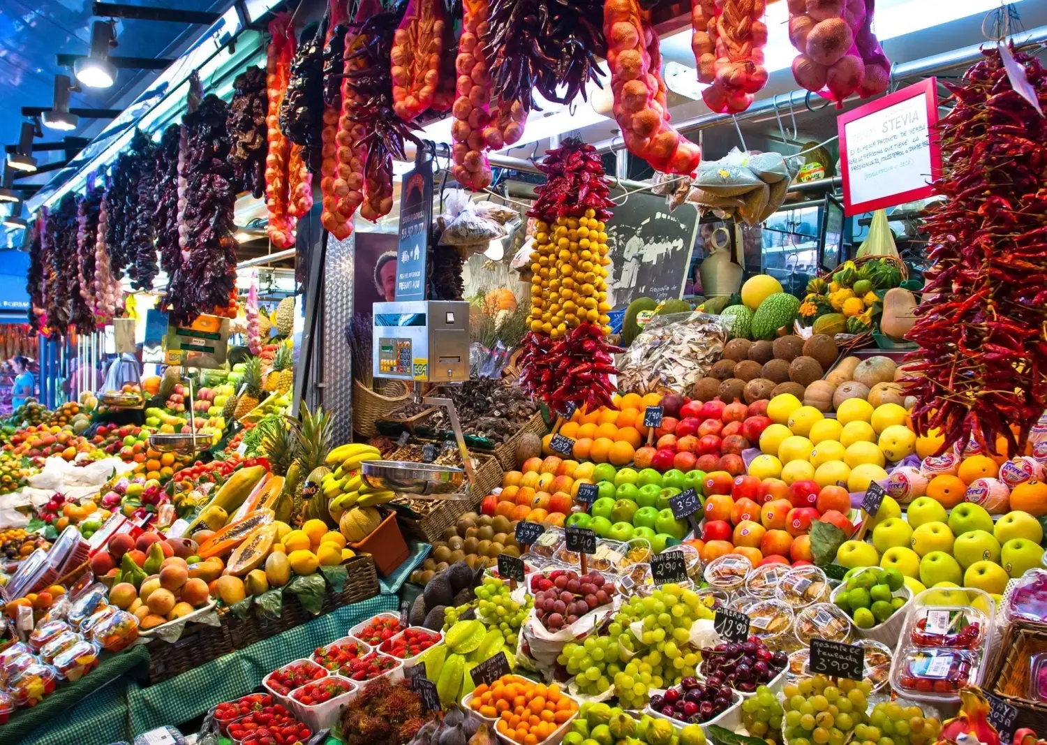 Vibrant produce stall inside La Boqueria Market in Barcelona, Spain displaying colorful hanging peppers and fresh fruits.