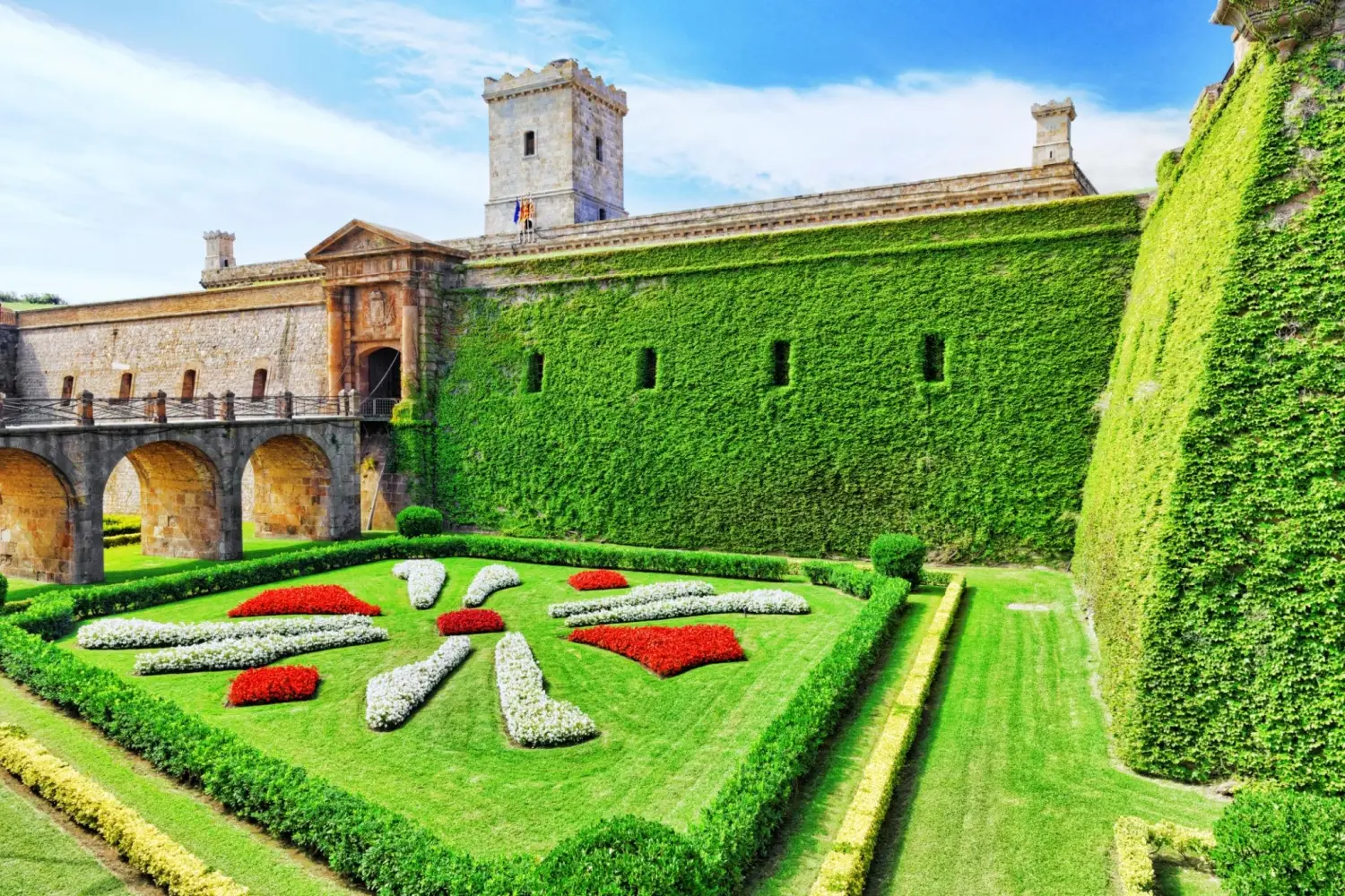 Montjuïc Castle in Barcelona, Spain, featuring ivy-covered stone walls and a landscaped flower garden in the moat.