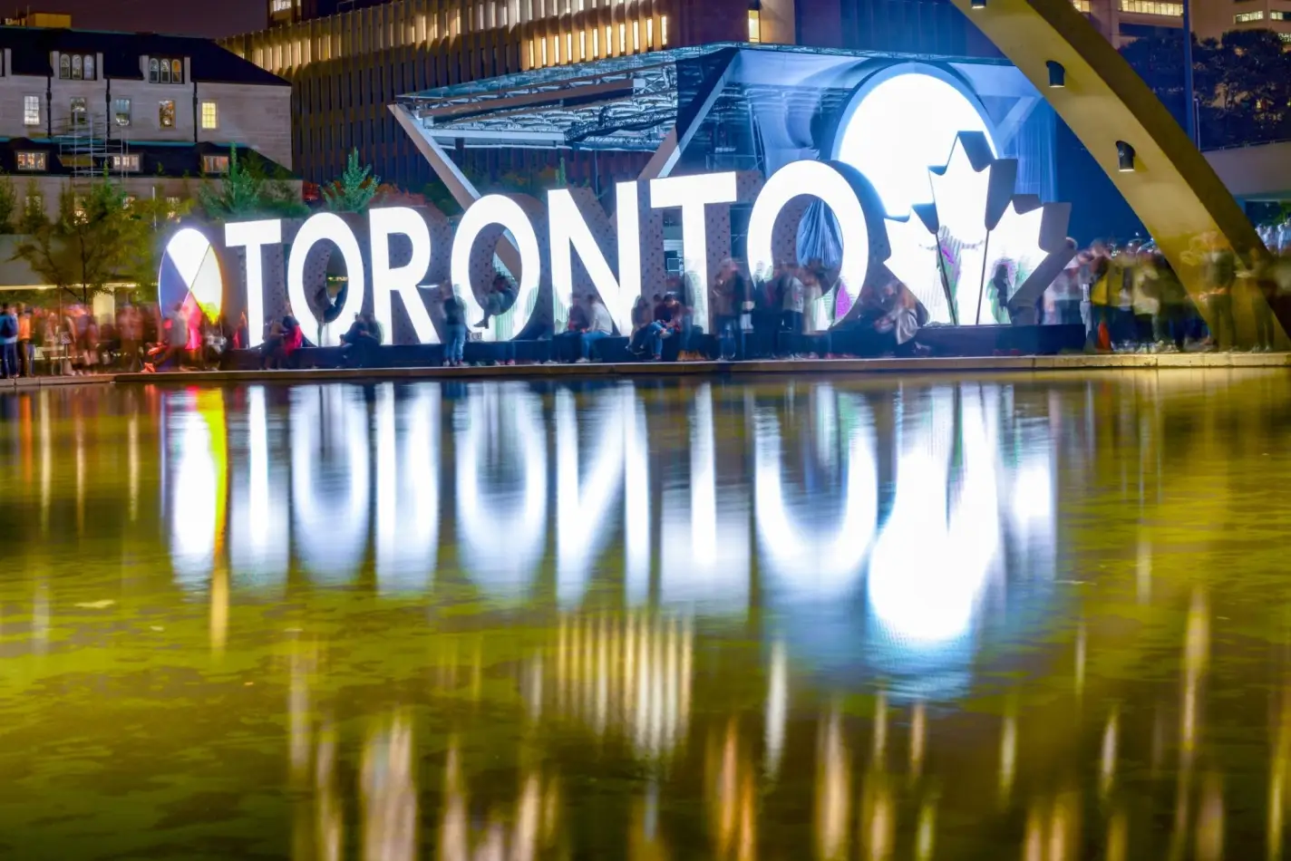 The famous illuminated Toronto sign at Nathan Phillips Square reflecting in the water at night.