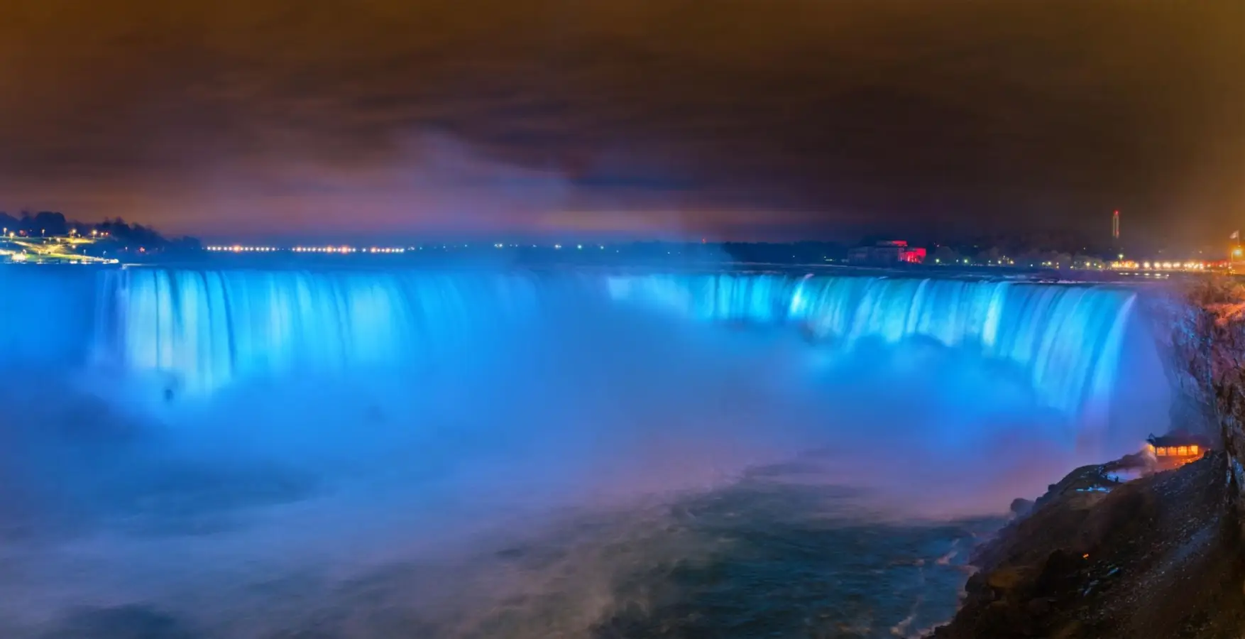 Niagara Falls Horseshoe Falls, also known as the Canadian Falls, illuminated in glowing blue light at night.