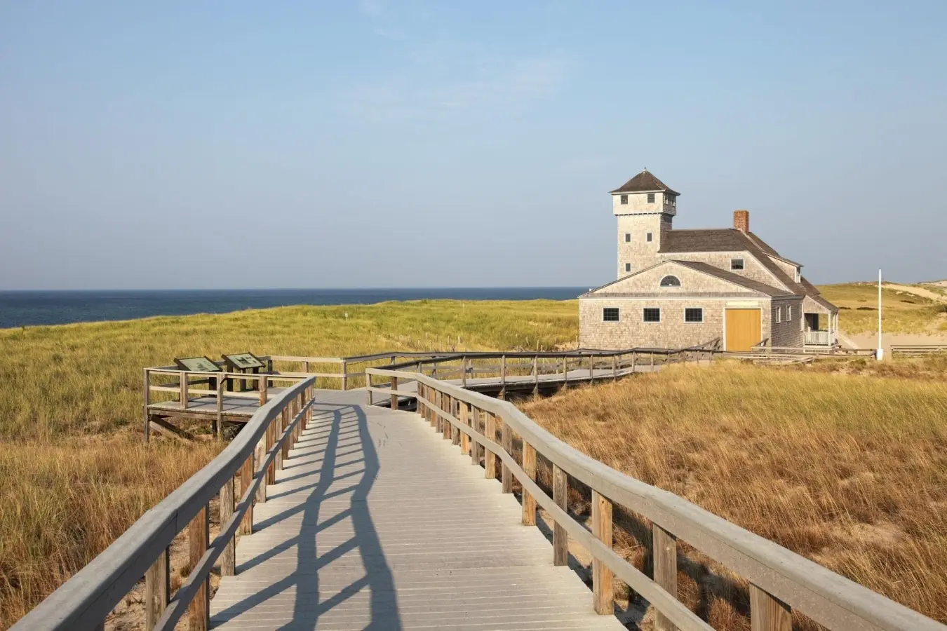Wooden boardwalk leading through coastal dunes toward the historic Old Harbor Life-Saving Station at Race Point Beach on Cape Cod, Provincetown, Massachusetts.