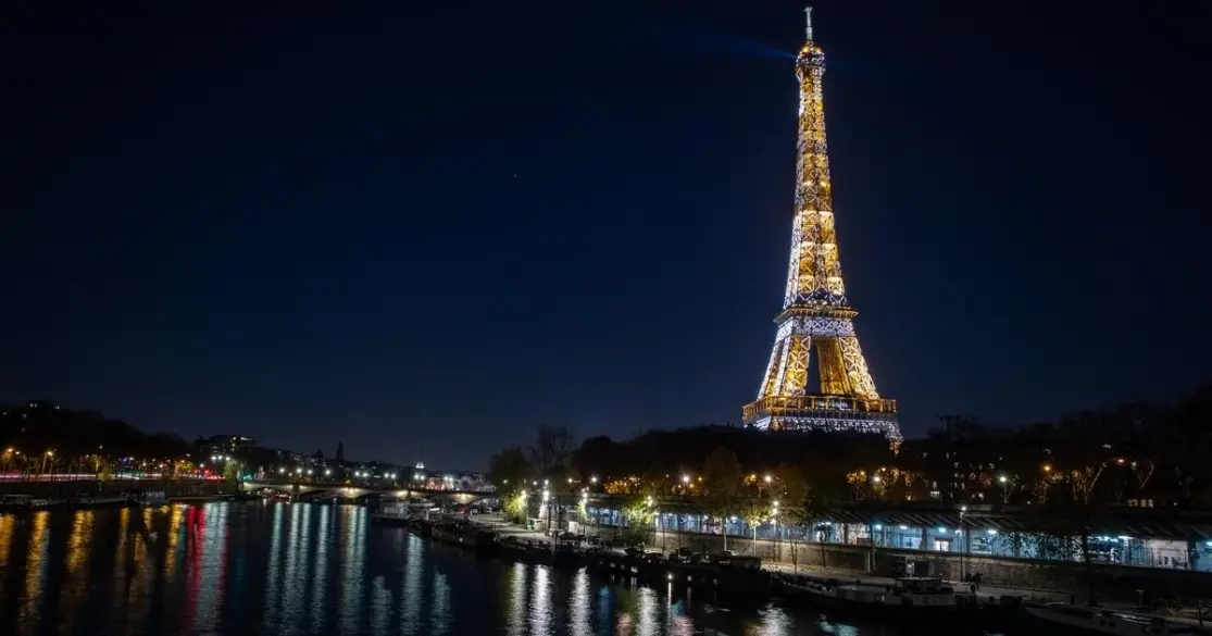 Eiffel Tower illuminated at night reflecting on the Seine River in Paris, France.