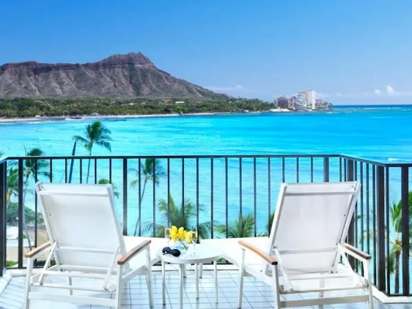 A luxury beachfront balcony view at the Halekulani Hotel, one of the best resorts in Waikiki, showcasing a clear turquoise ocean and the Diamond Head crater.