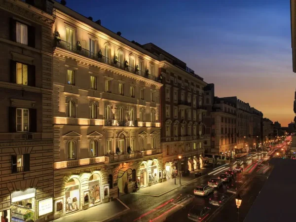 Exterior of Hotel Artemide illuminated at dusk on Via Nazionale in Rome, Italy, with traffic blurred by motion on the street below.