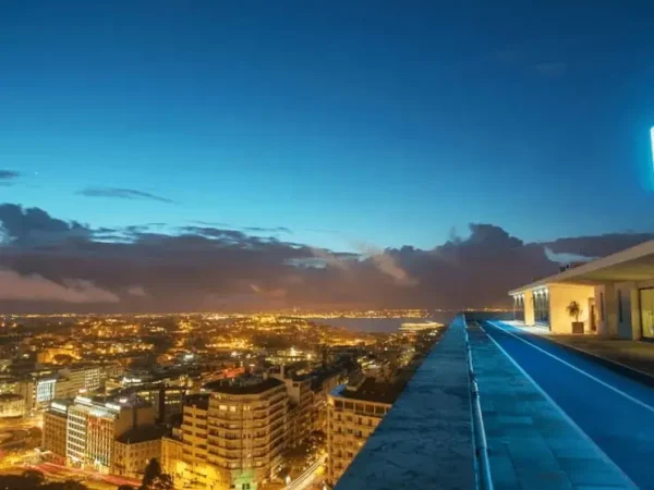 A wide, high-angle twilight view of Lisbon, Portugal, taken from a rooftop terrace featuring a blue outdoor running track.