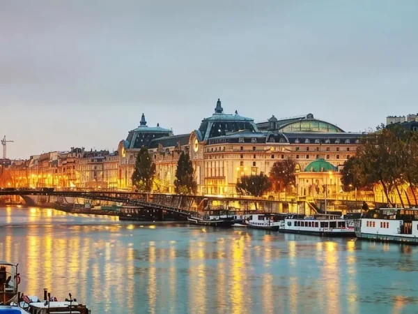 Paris evening view of the lit-up Musee d'Orsay museum and Passerelle Leopold-Sedar-Senghor bridge over the Seine River.