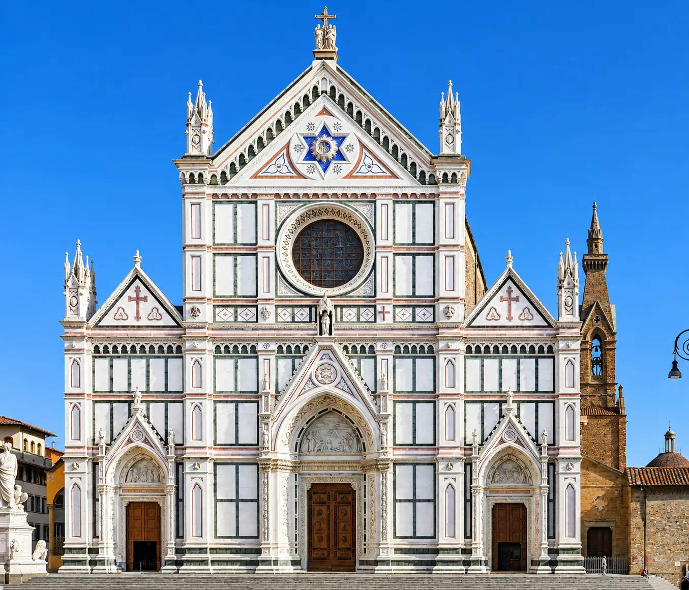 Front marble facade of the Basilica di Santa Croce in Florence, Italy, featuring its neo-Gothic geometric architecture and central rose window against a clear blue sky