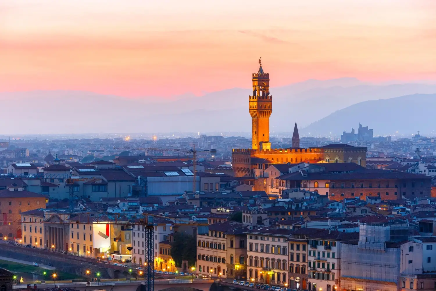 Panoramic view of the Florence skyline at sunset featuring the illuminated Torre Arnolfo of Palazzo Vecchio.