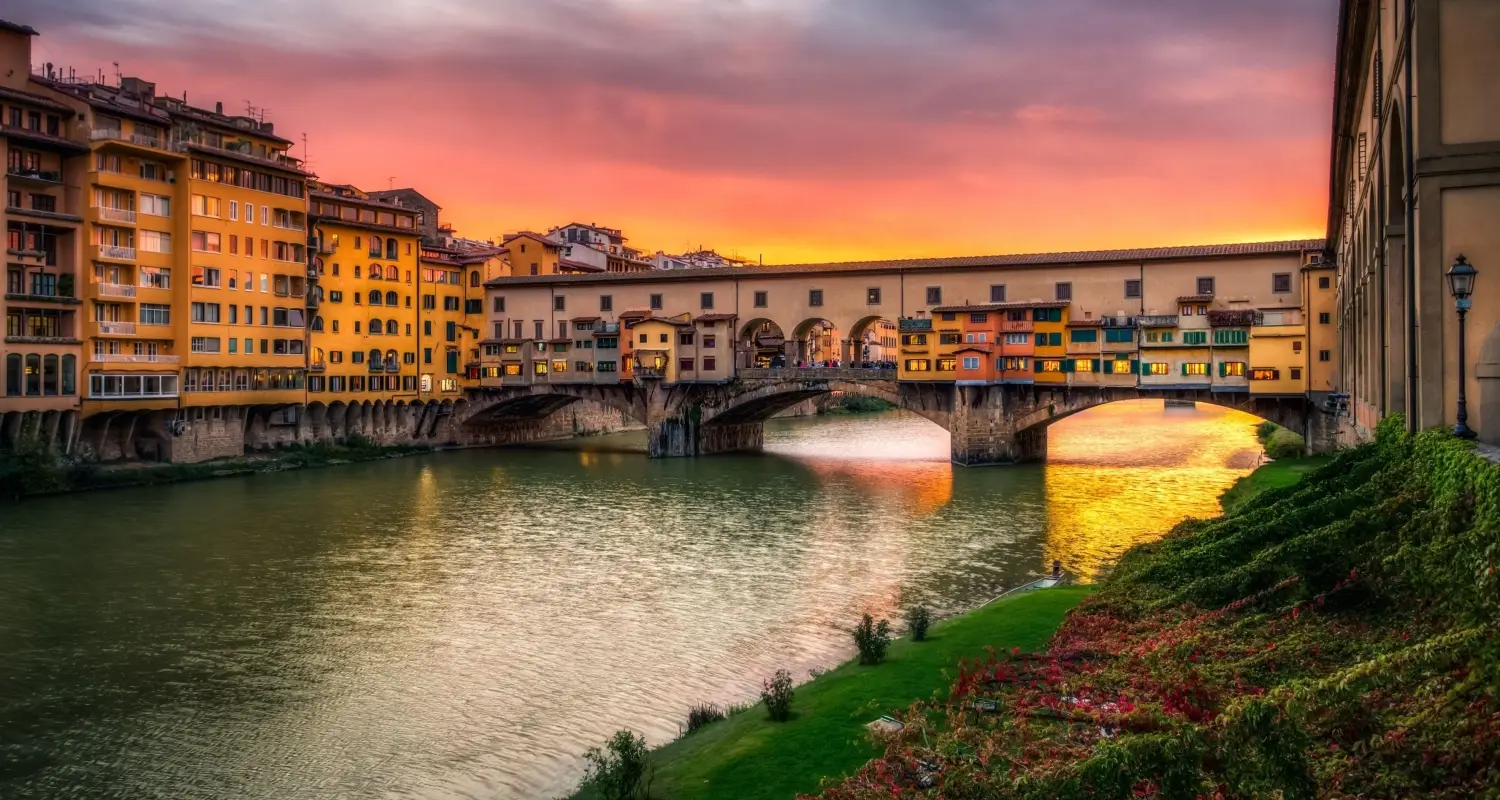 Ponte Vecchio bridge over the Arno River in Florence, Italy at sunset with colorful shops.