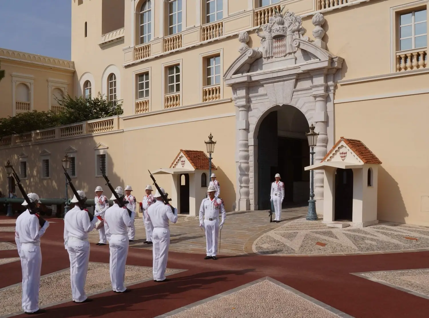 Monaco guards in summer white uniforms march outside the Prince's Palace facade during the daily changing of the guard ceremony.