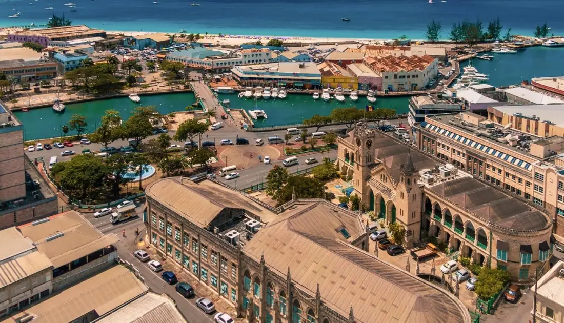 Aerial view of the Bridgetown waterfront and Careenage marina in Barbados featuring historic colonial buildings, boats docked in turquoise water, and a coastal city landscape.