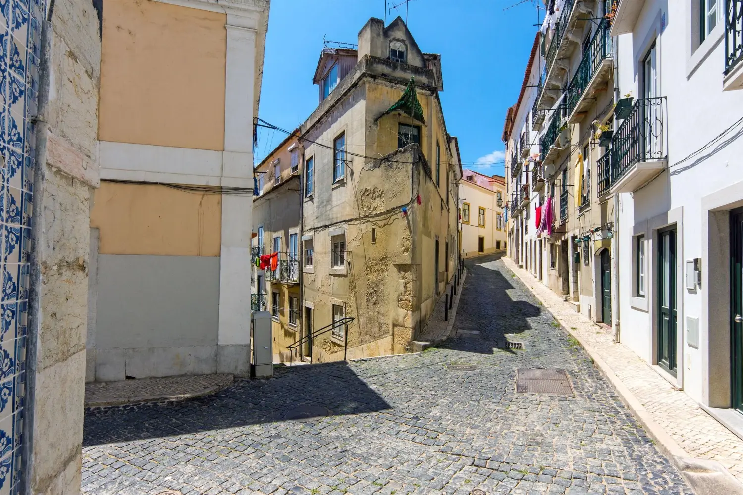 A narrow cobblestone alleyway in the historic Alfama district of Lisbon, Portugal, known for its maze-like streets and long history dating back to Moorish times.