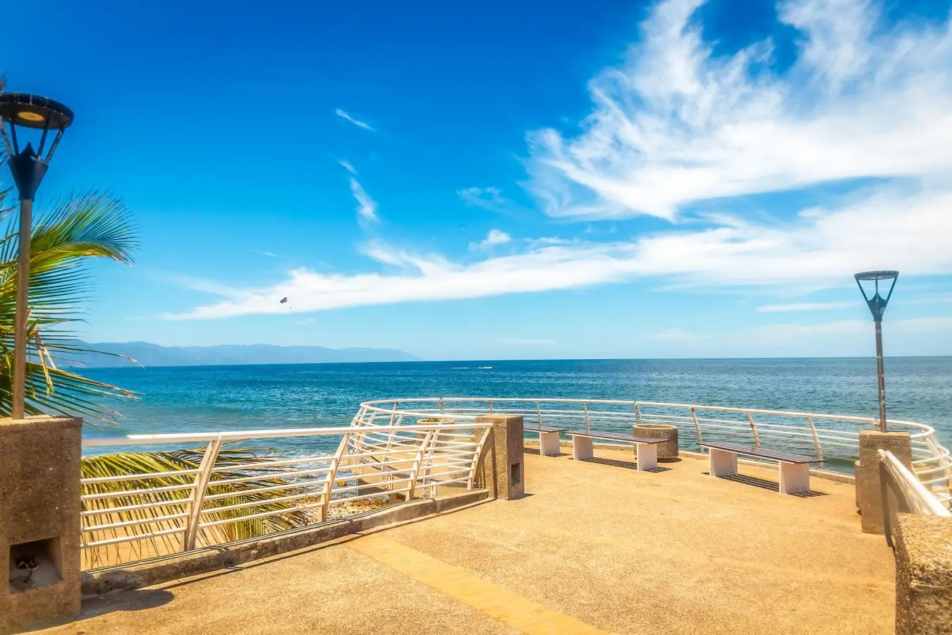 Ocean viewpoint on the Puerto Vallarta Malecon boardwalk with white railings and benches under a bright blue sky in Jalisco, Mexico.