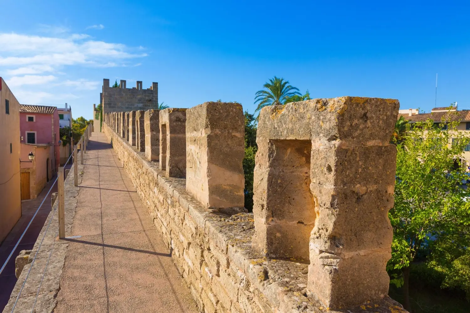 A scenic view along the walkable stone pathway on top of the medieval fortress walls in Alcudia Old Town, Mallorca, Spain under a clear blue sky.