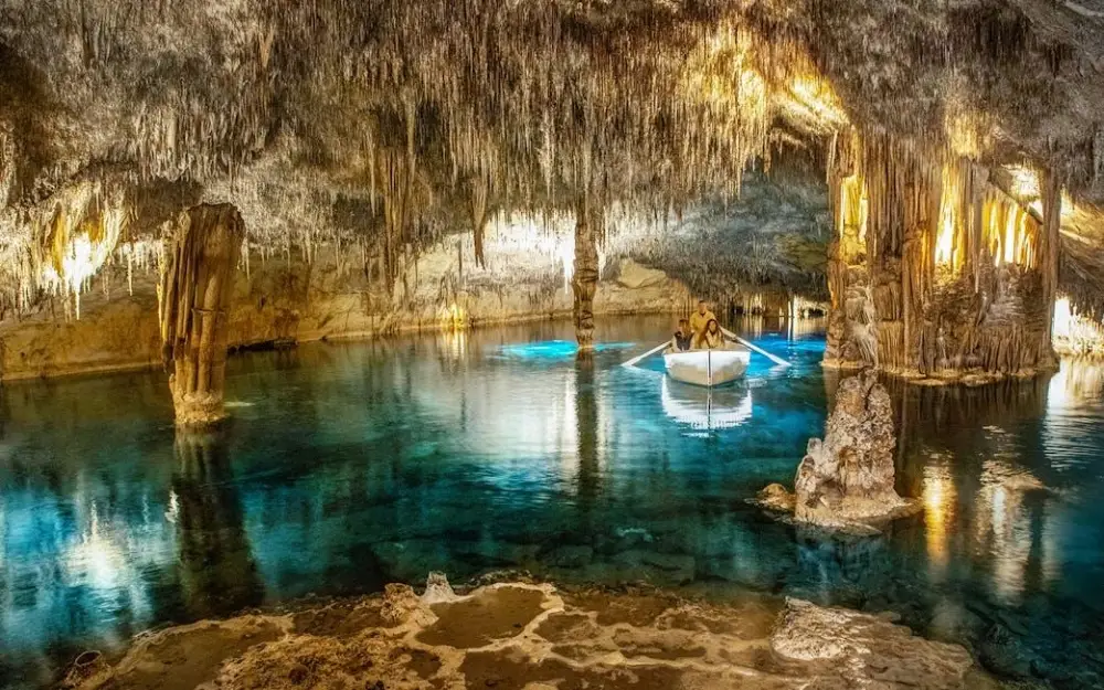 A small tourist boat floating on the clear turquoise water inside the illuminated Drach Caves in Porto Cristo, Mallorca, Spain.