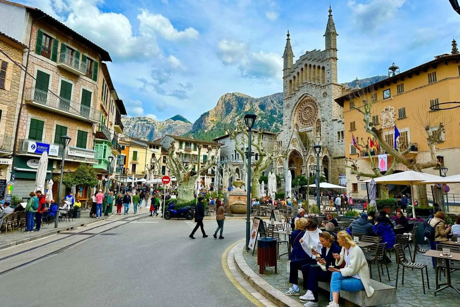 Colorful historic square of Placa de la Constitucio in Soller, Mallorca, Spain, with the Church of Sant Bartomeu and Serra de Tramuntana mountains.
