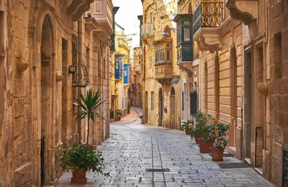 A narrow cobblestone street lined with traditional limestone buildings and balconies in Birgu, Malta.