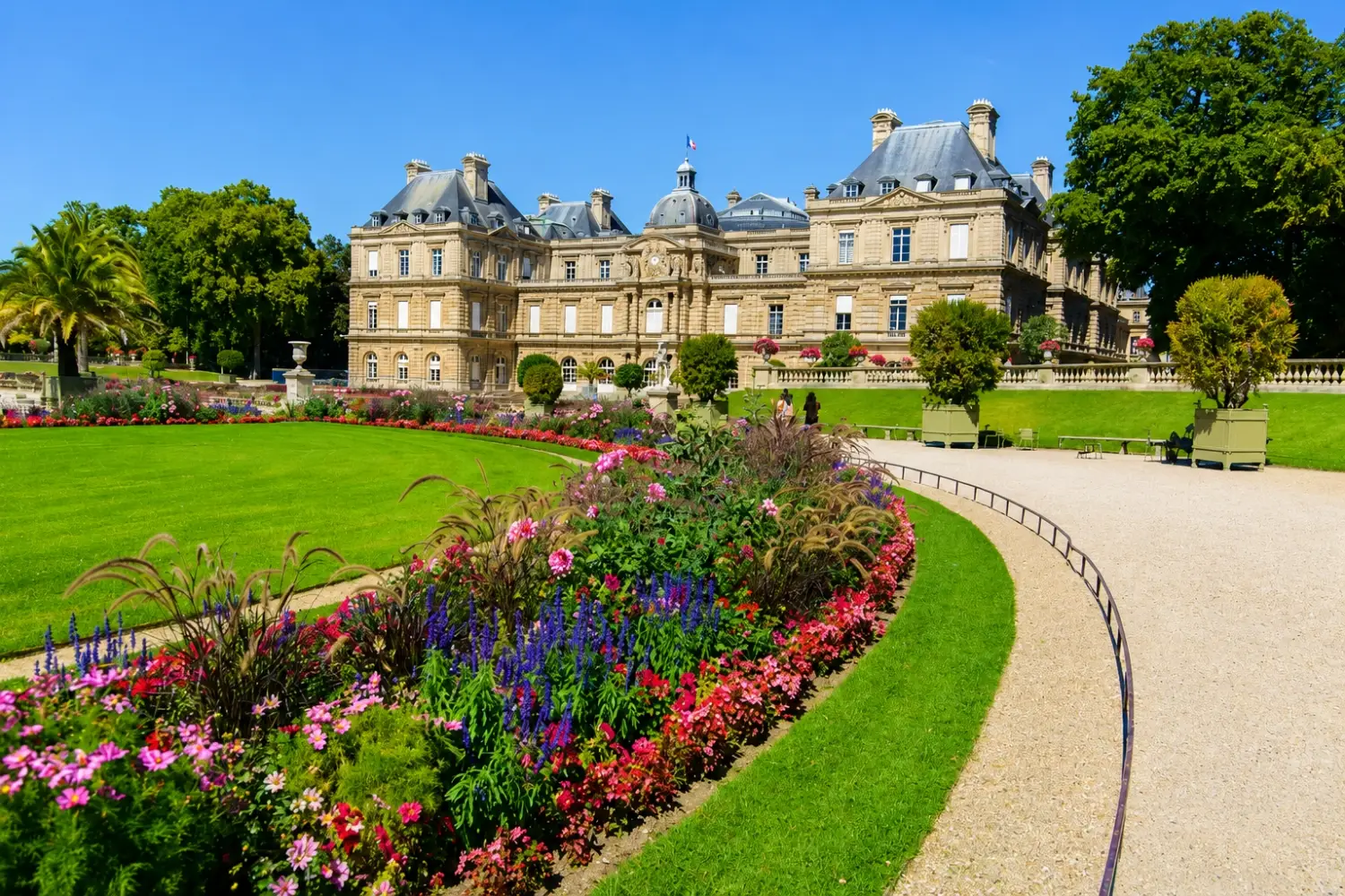 Vibrant flower beds and a pathway in the Luxembourg Gardens, or Jardin du Luxembourg, in Paris with the iconic Luxembourg Palace in the background.