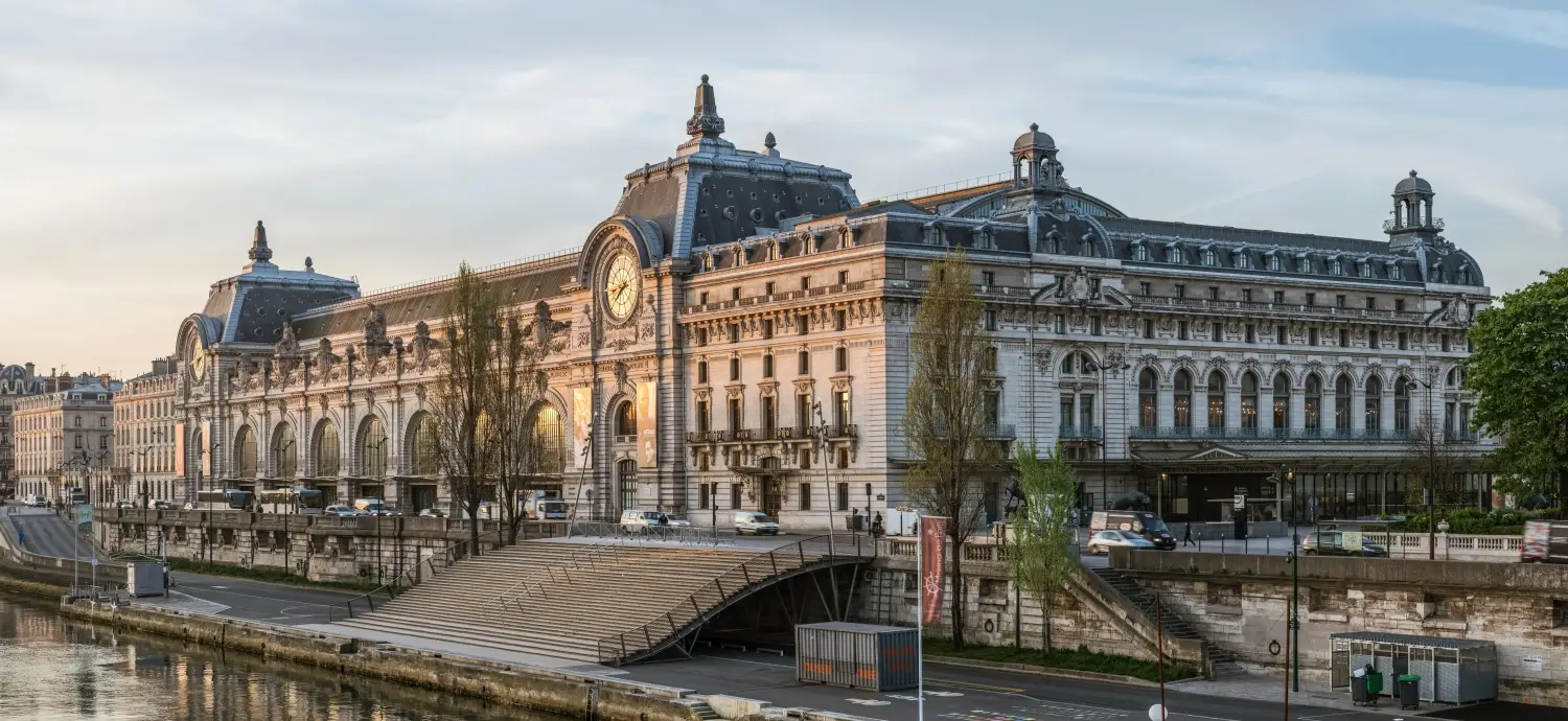 The exterior facade of the Musee d'Orsay in Paris, a renowned art museum housed in a repurposed Belle Époque train station along the Seine River.