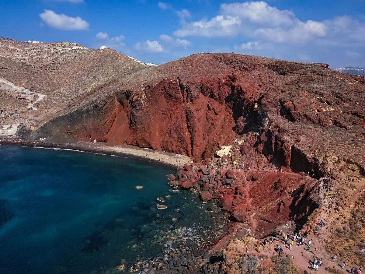 Red Beach Santorini aerial perspective showing red volcanic rock cliffs and dark sand coastline.