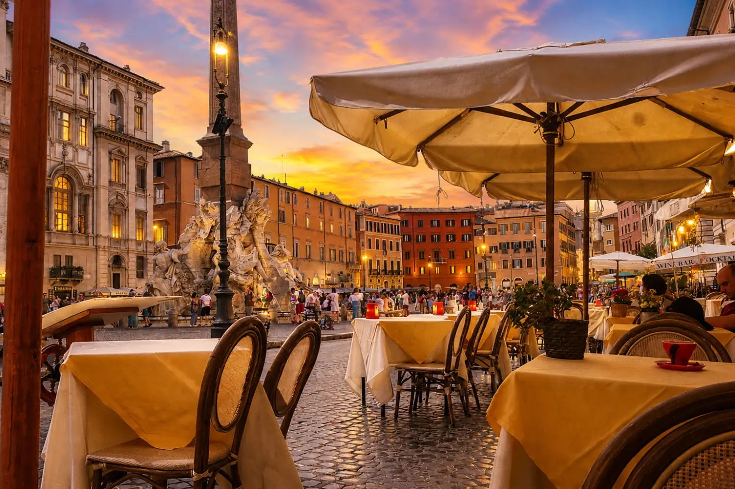 Outdoor restaurant seating with yellow tablecloths looking towards Bernini's Fountain of the Four Rivers in Piazza Navona, Rome at sunset.