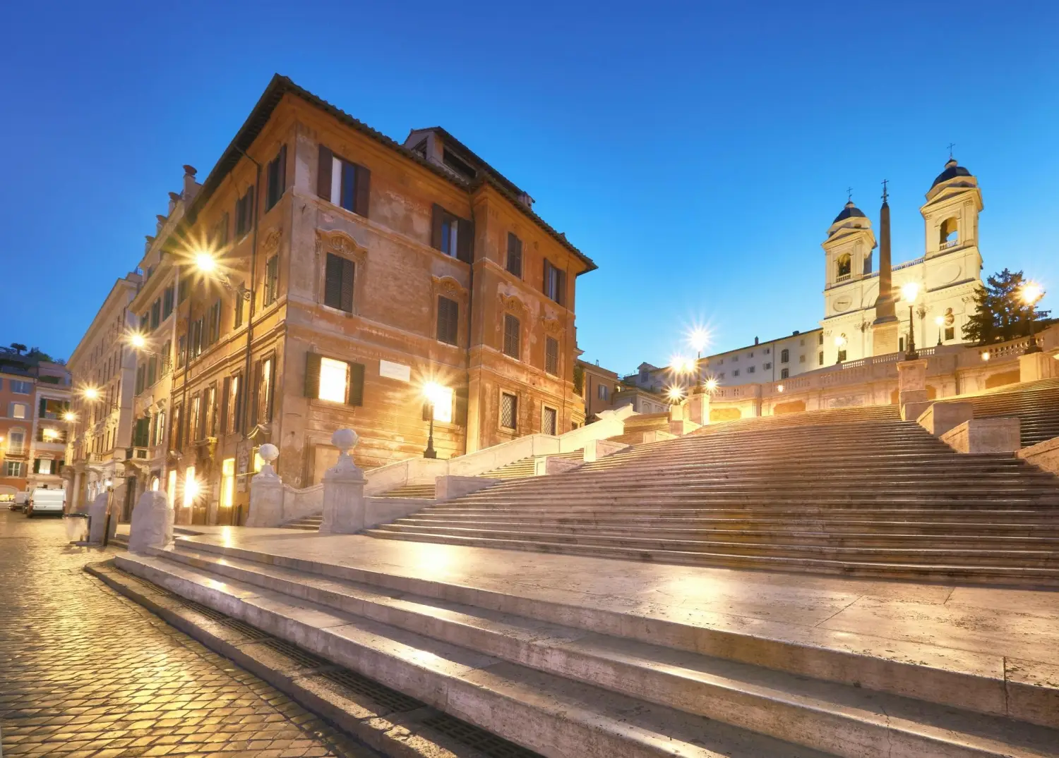 The Spanish Steps in Rome at dusk with the illuminated Trinità dei Monti church overlooking the Piazza di Spagna.