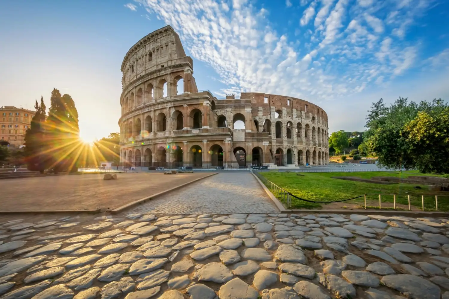Sun shining over the historic Roman Colosseum elliptical amphitheater, Rome, Italy with a stone cobblestone path.