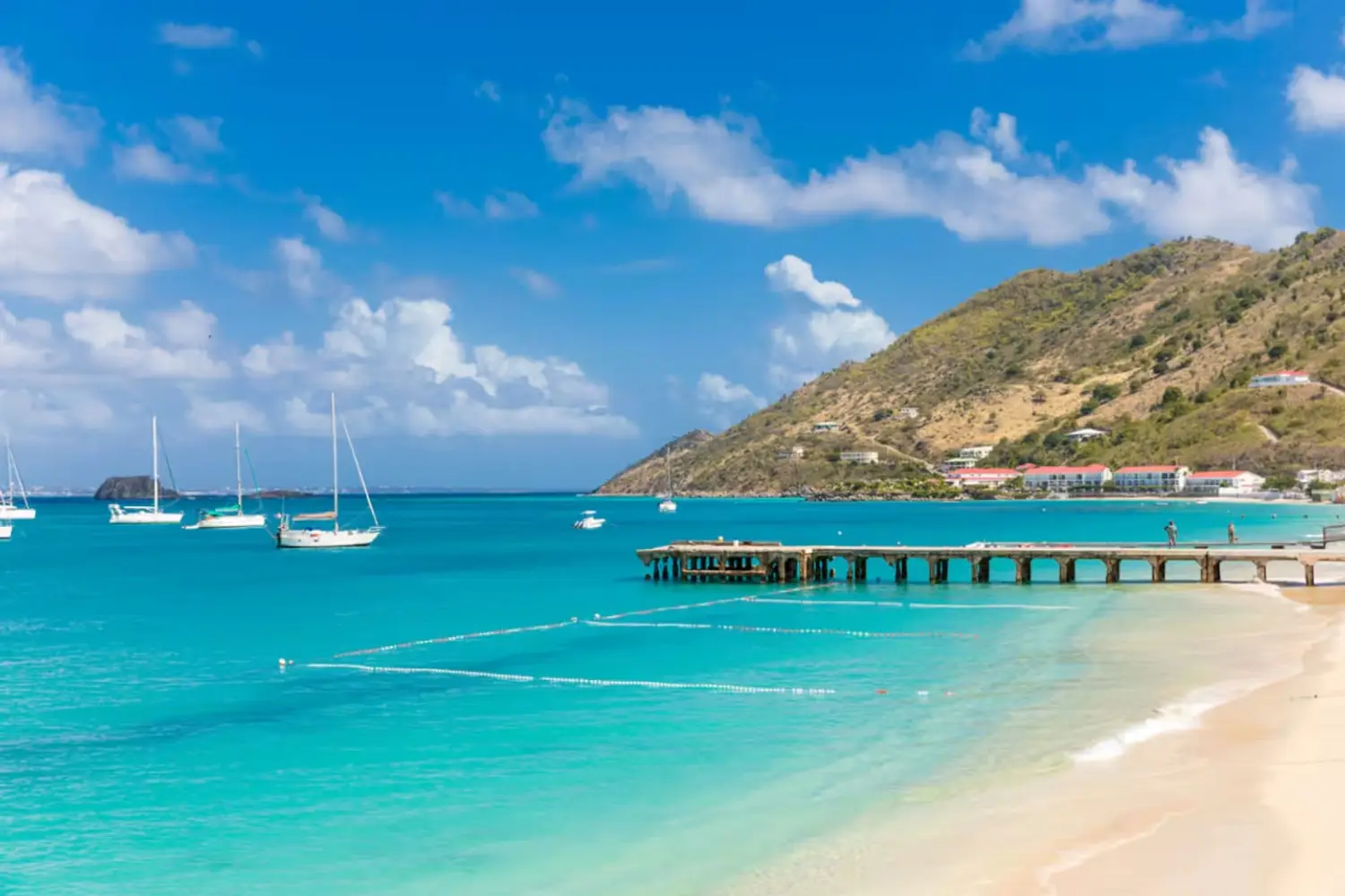 Wooden pier and boats anchored in the turquoise water of Grand Case Beach in Saint Martin.