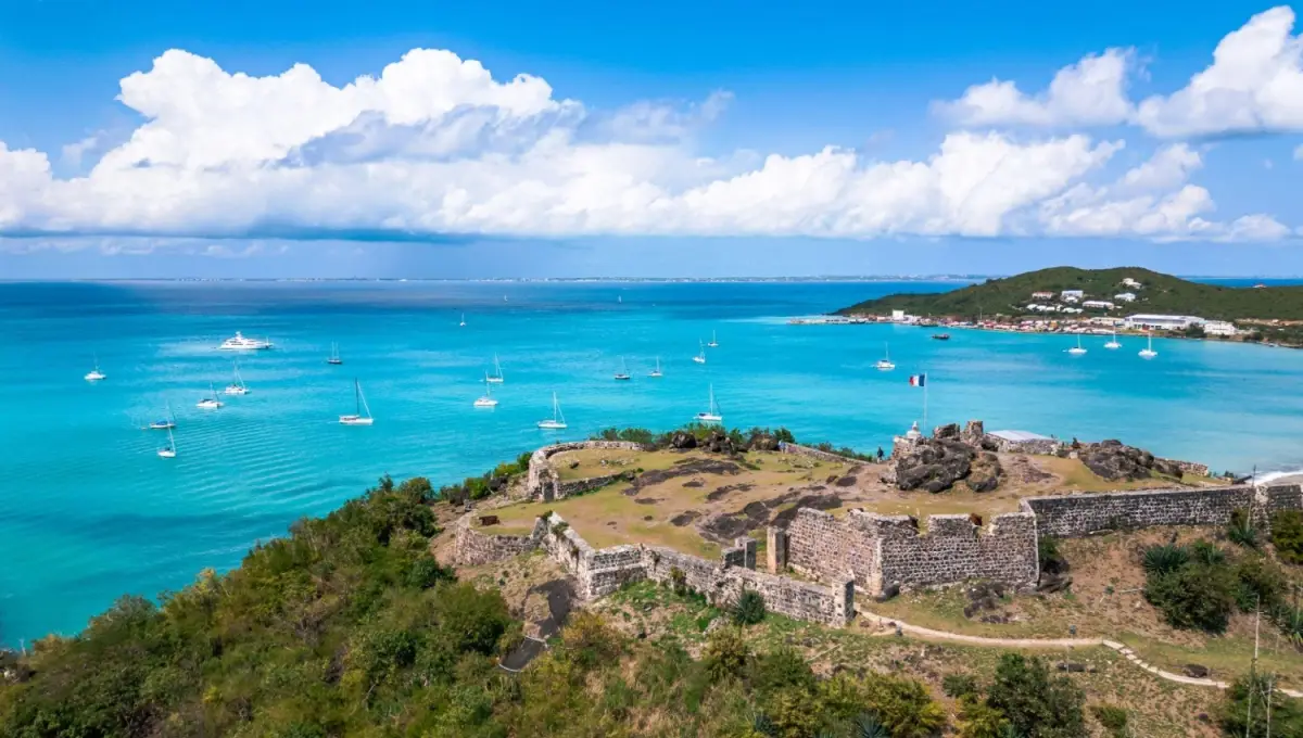 Stone ruins of Fort Louis Saint Martin on a hill overlooking sailboats in the turquoise Caribbean Sea.