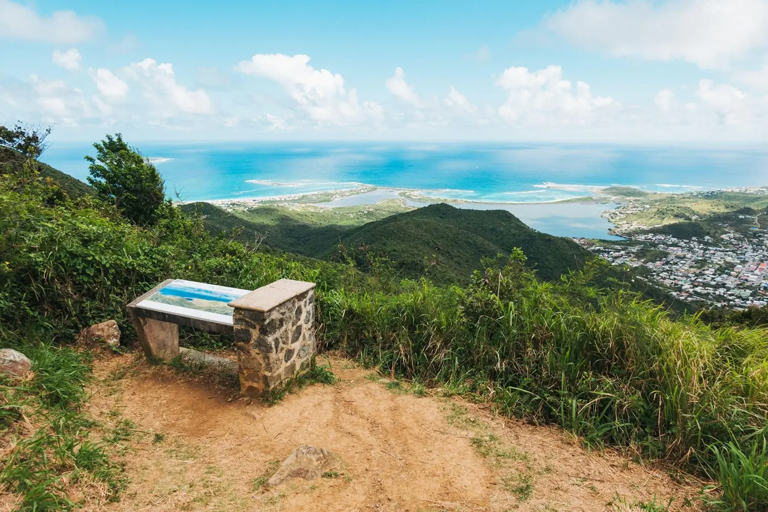 Panoramic view from Pic Paradis (Paradise Peak) hiking trail showing an information plaque on the highest peak of Saint Martin in the Caribbean, overlooking coastal areas like Marigot and Grand Case.