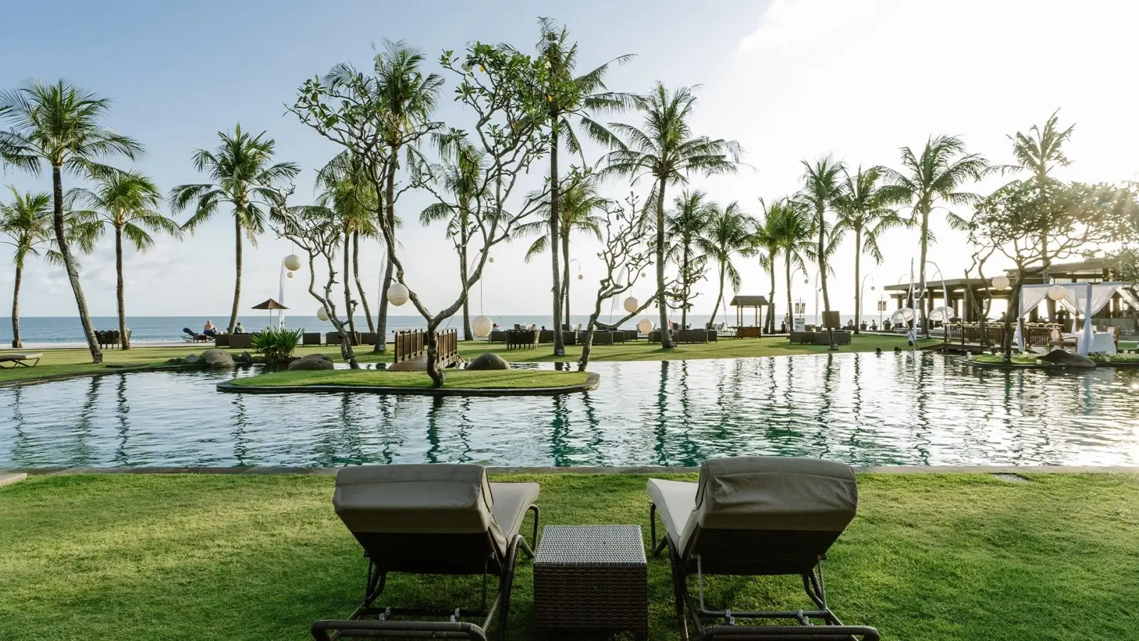 Luxury beachfront pool with lounge chairs and palm trees at a tropical resort in Bali.