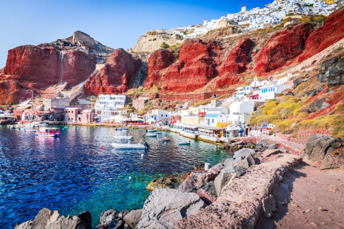 Ammoudi Bay port in Santorini Greece with boats in clear blue water and red volcanic cliffs below Oia village.