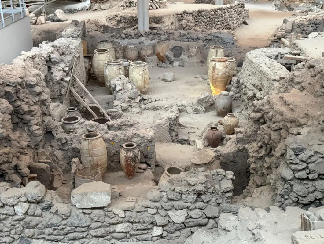 Ancient Minoan ruins of Akrotiri in Santorini Greece showing preserved stone walls and large clay storage jars called pithoi.