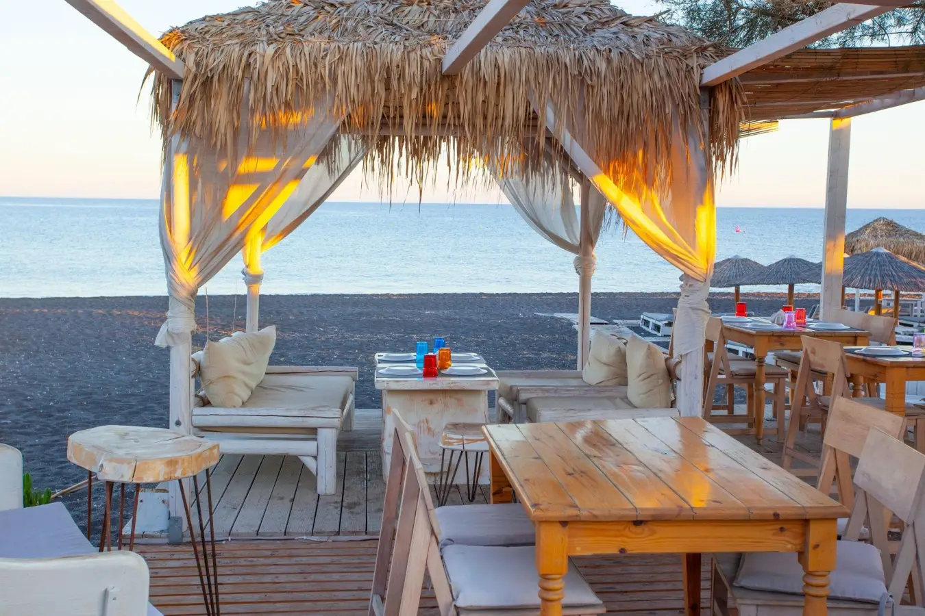 Seaside restaurant cabana with lounge seating on the black sand beach of Perissa in Santorini, Greece.