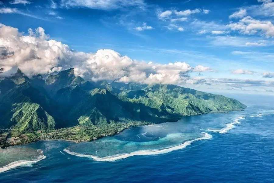 Aerial view of lush green mountains and coral reefs in Teahupo'o, Tahiti, French Polynesia.