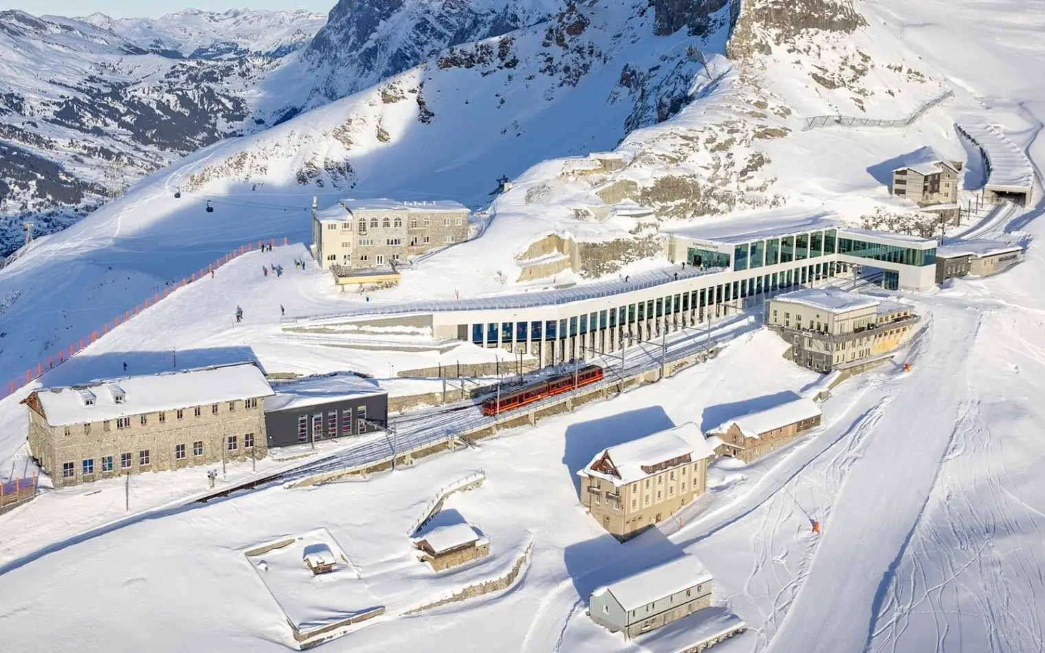 A red mountain train arriving at the modern Eiger Glacier station in Switzerland amidst snowy peaks.