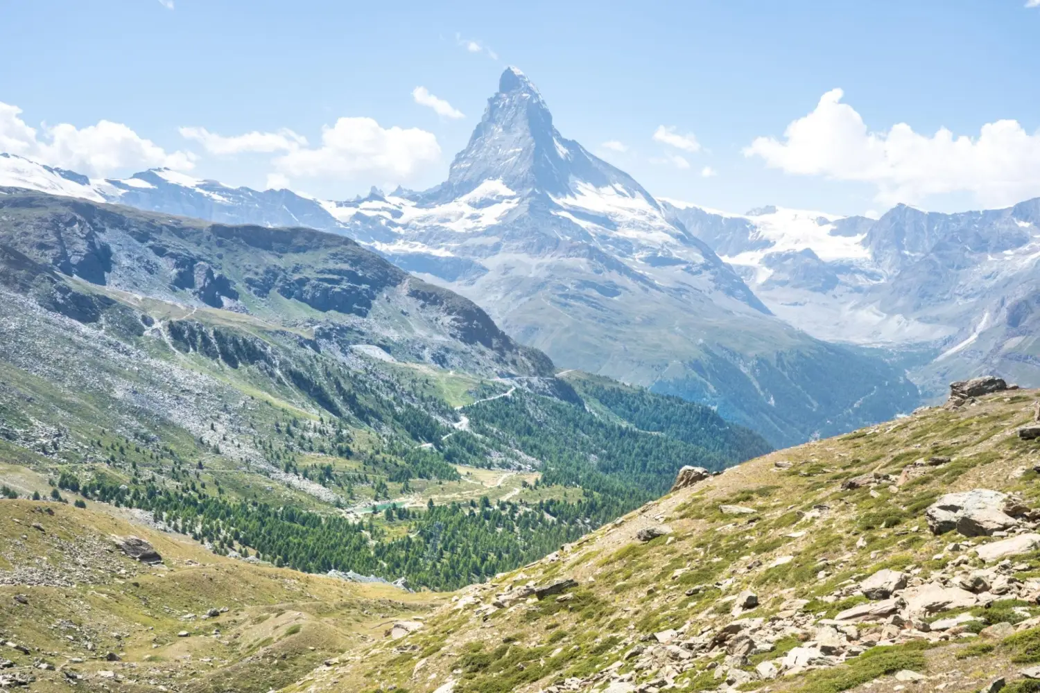 Scenic summer view of the iconic Matterhorn mountain peak rising above a green alpine valley near Zermatt, Switzerland.