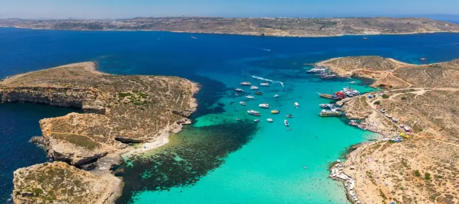 The Blue Lagoon on Comino Island, Malta, showcasing crystal-clear turquoise waters, boats anchored in the bay, and rugged coastline.