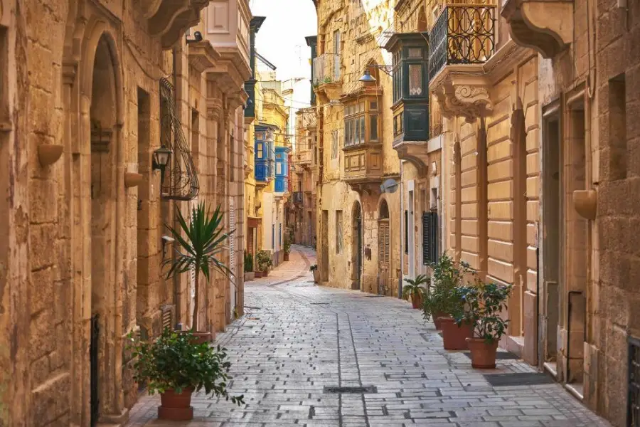 Narrow stone alleyway with traditional enclosed wooden balconies and potted plants in the historic city of Birgu, Malta.